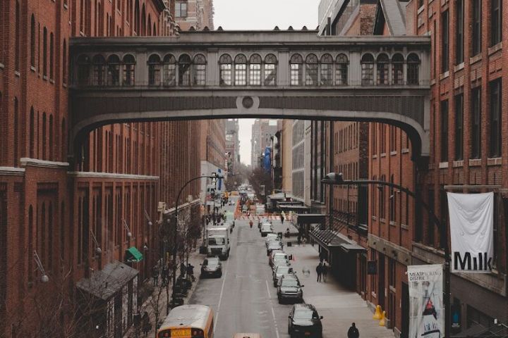 Urban street with yellow taxis, school bus, and brick buildings, bridge above street.