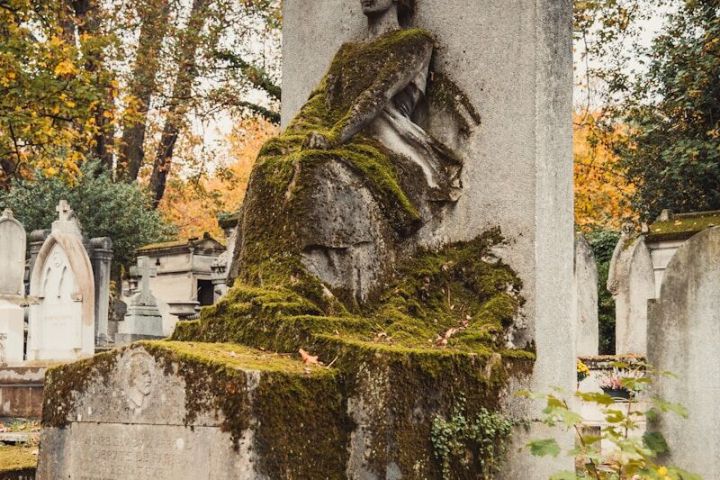Moss-covered stone statue in a cemetery surrounded by autumn trees.