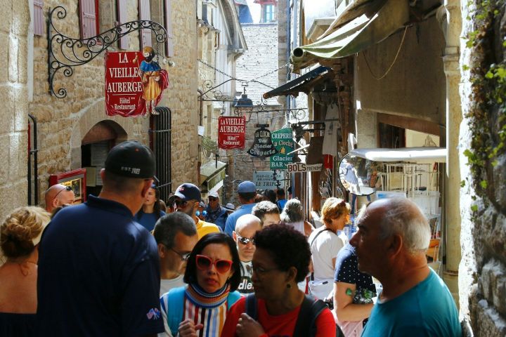 Crowded narrow street with tourists, shops, and signs in a historical European town.