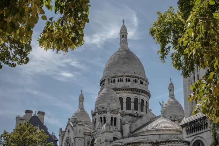 Sacre-Coeur Basilica framed by green trees under a blue sky.