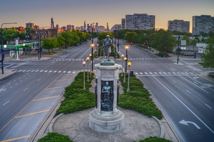 Symmetrical view of a monument with a city skyline in the background at sunset.