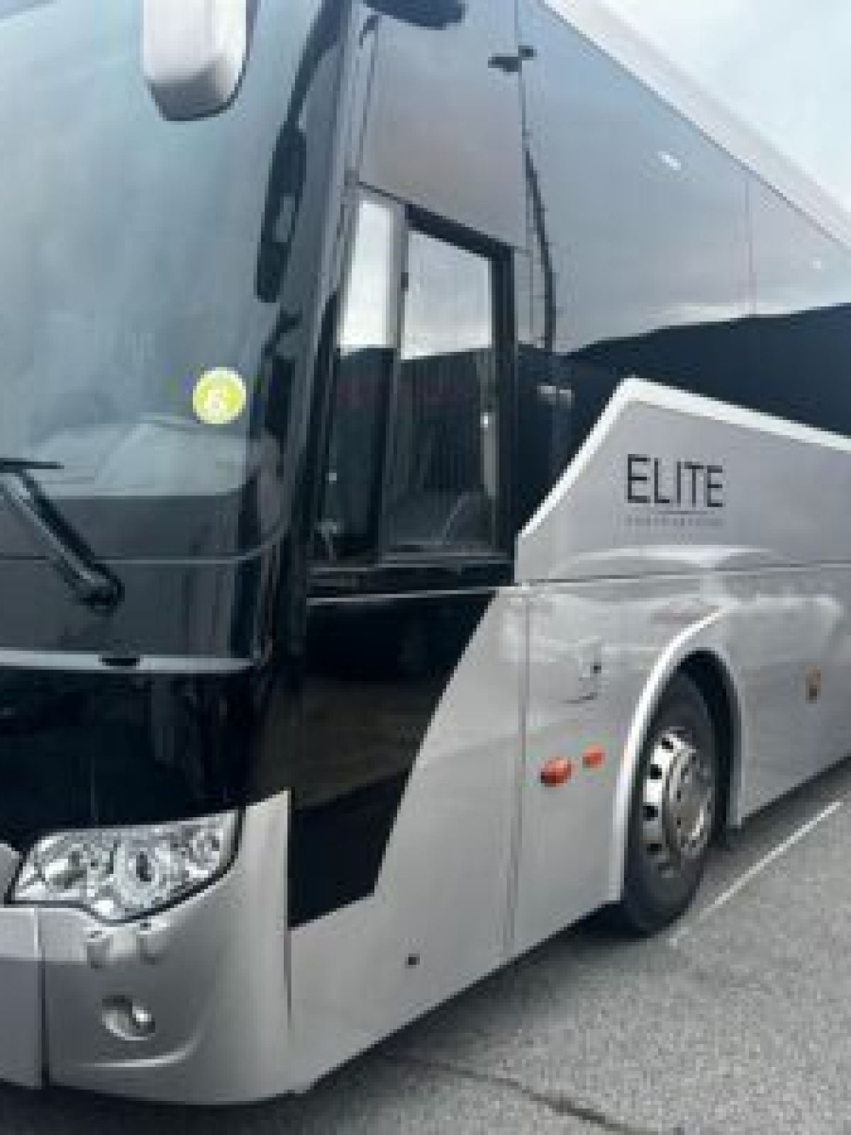 Silver and black tour bus parked in a lot with 'Elite' signage.