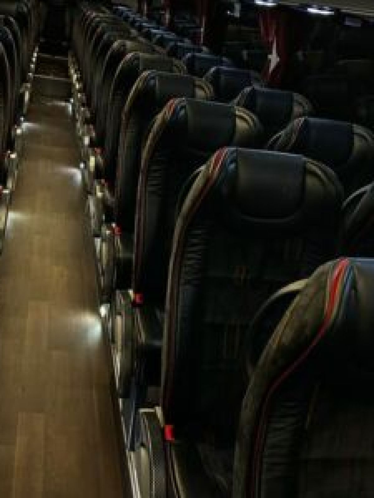 Empty bus interior with rows of black seats and a central aisle.