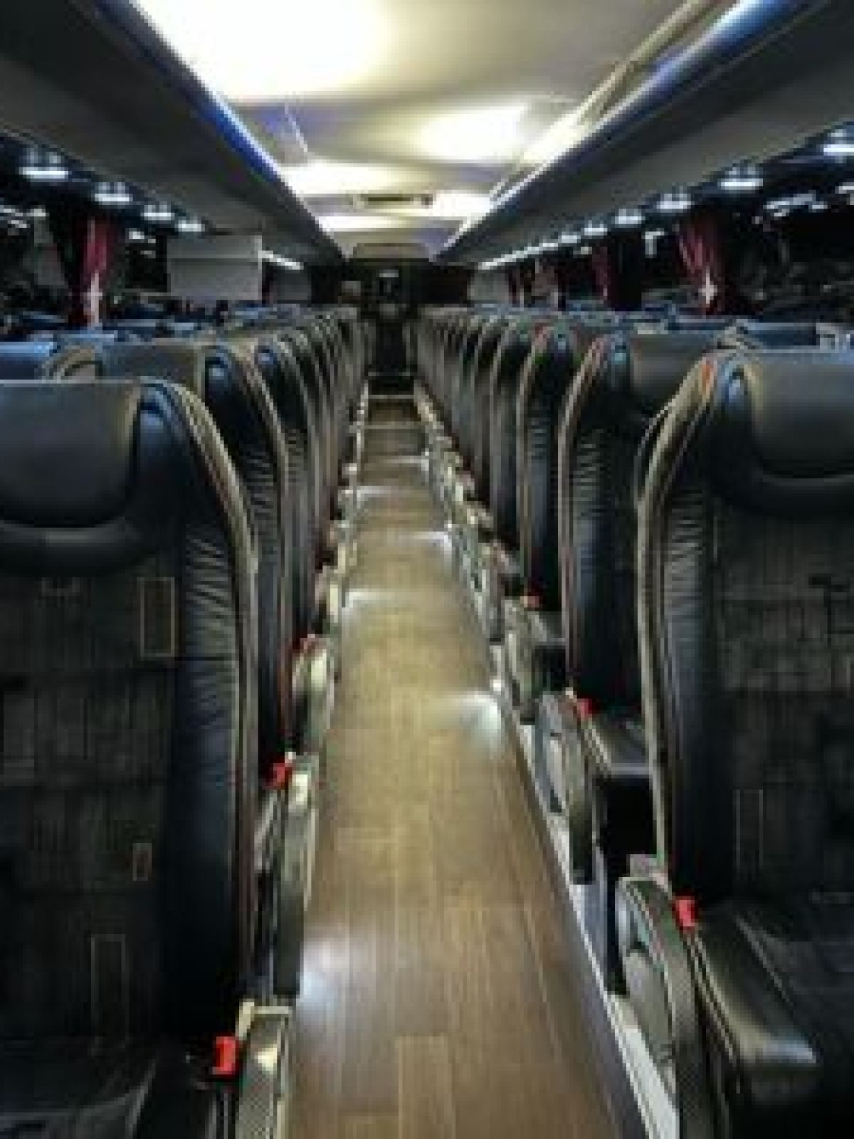Empty coach bus interior with rows of black seats and overhead lighting.