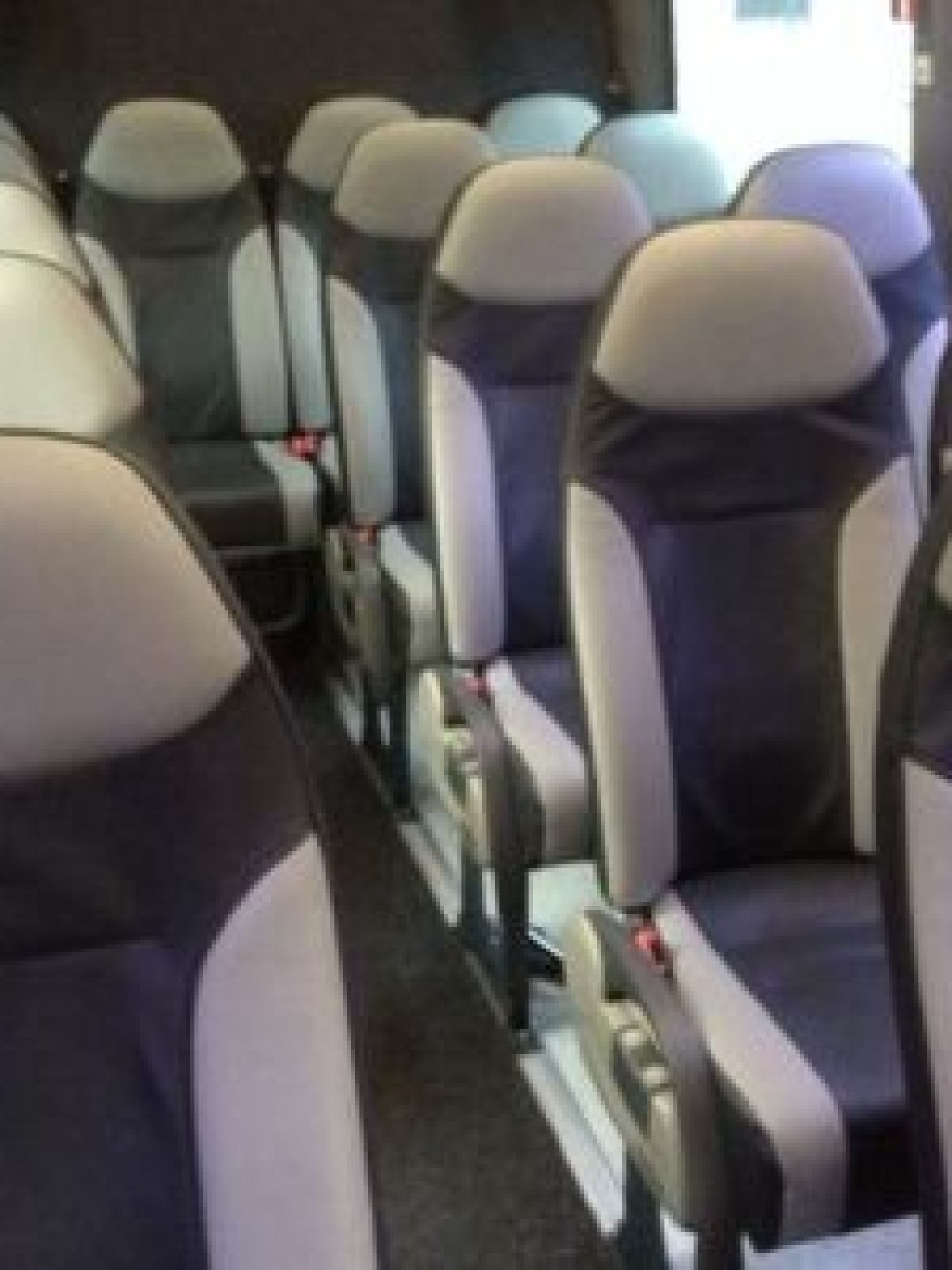 Interior of a small bus with rows of empty grey and black seats.