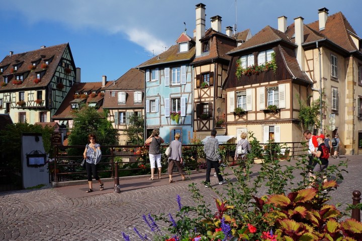 People walking near colorful half-timbered houses in a European village.