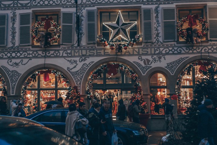 Festive street scene with decorated building, wreaths, star, and people walking.