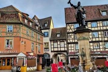 Charming European square with timber-framed buildings and a statue in the center.
