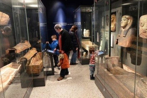 People observe ancient sarcophagi in a museum exhibit.