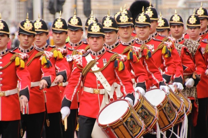Marching band in red uniforms with helmets and drums in a parade.