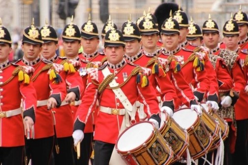 Marching band in red uniforms with drums in a ceremonial parade.