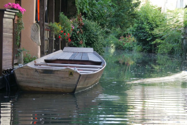 Wooden boat on a calm canal beside a building with colorful flowers.