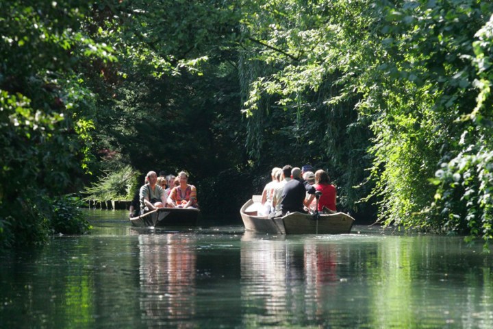 People in boats paddling through a lush, green, tree-lined canal.