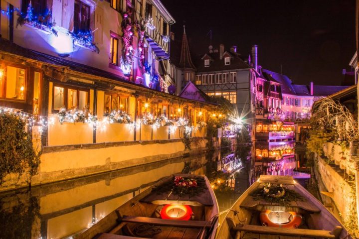 Nighttime view of lit-up canal with festive lights on buildings and boats.