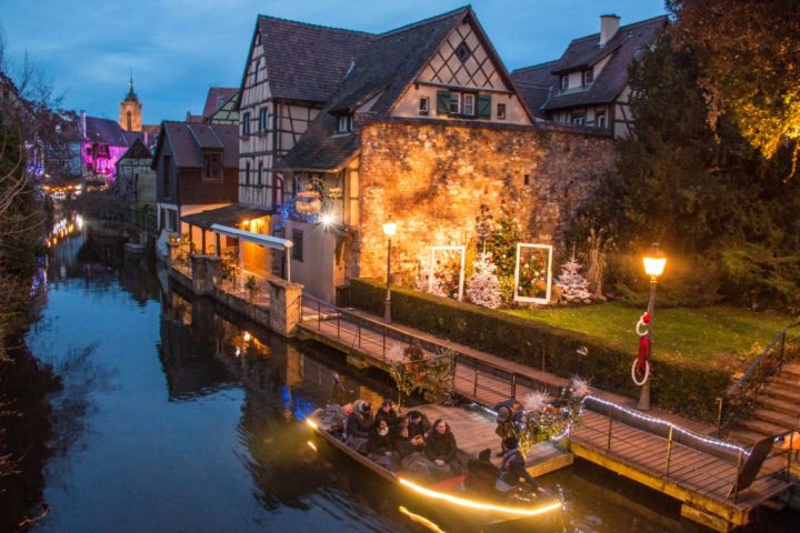 Evening boat ride on canal past decorated half-timbered houses with festive lights.