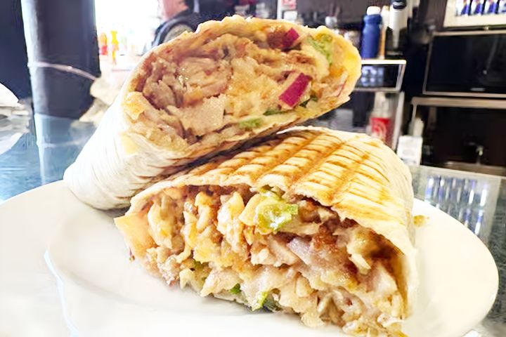 Grilled chicken wrap with vegetables cut in half on a white plate.