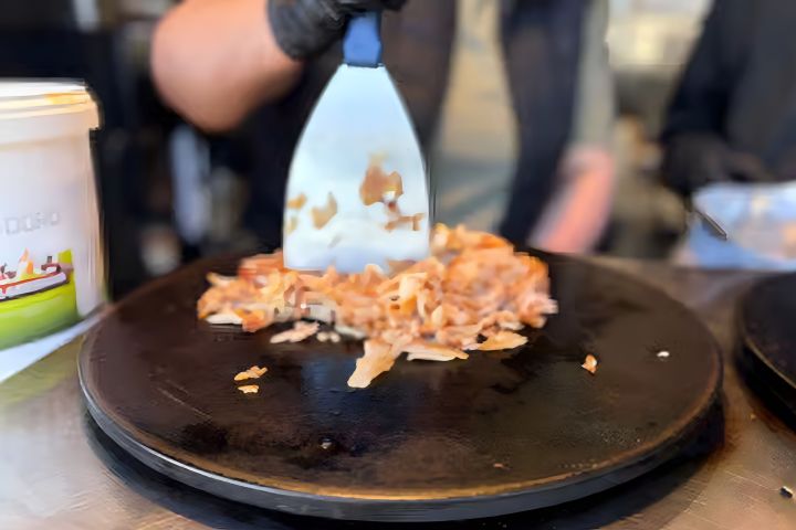Person uses spatula to flip chopped ingredients on a hot grill.