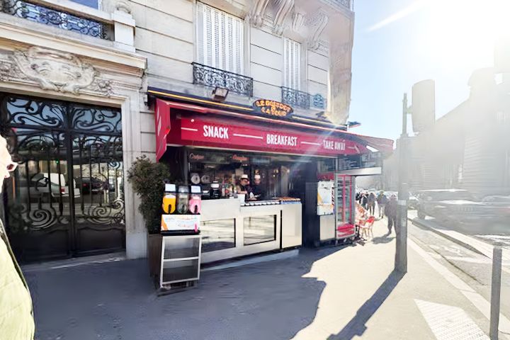 Street-side cafe with red awning offering snacks and breakfast with people outside.
