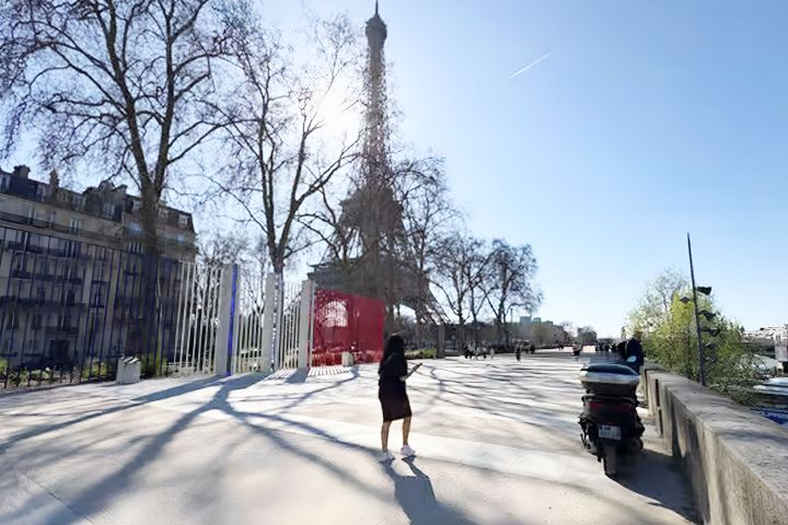 Person standing near Eiffel Tower with clear sky and shadowed sidewalk.