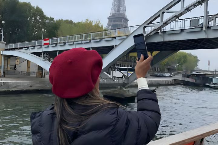 Person in red beret taking photo near bridge with Eiffel Tower in background.