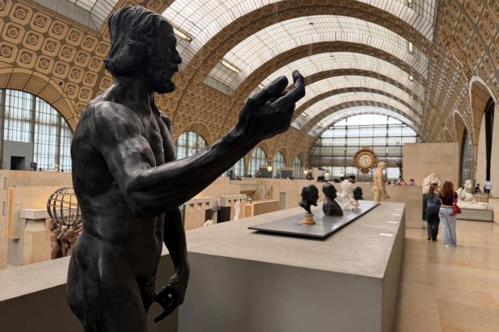 Museum interior with sculptures and arched ceiling, featuring a prominent statue in the foreground.
