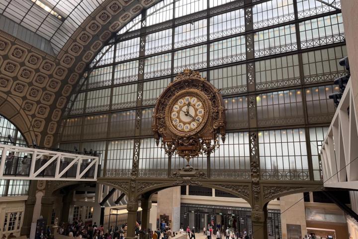 Large ornate clock in a grand hall with arched glass ceiling.