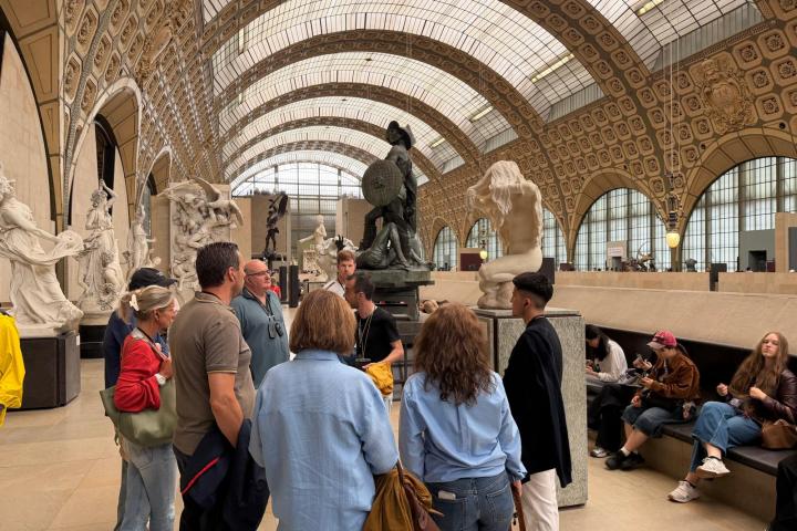 Group of people in a large hall with sculptures and ornate arched ceiling.