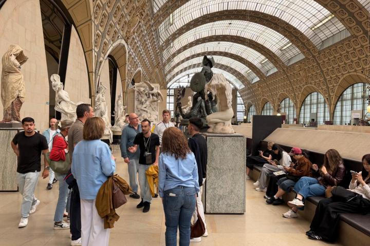 Group of people in a museum with statues and vaulted glass roof.