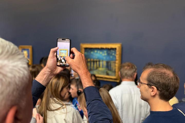 Crowd in a gallery, person photographing a painting with a phone.