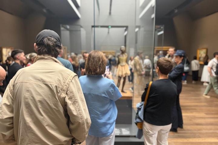 Visitors view a museum sculpture in a crowded gallery with paintings on the walls.