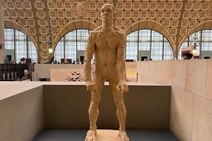 Stone statue of a standing man in a museum with arched windows.