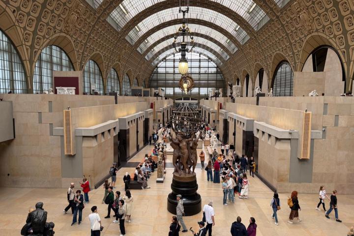 People walking in a large, ornate museum hall with high arched ceilings.