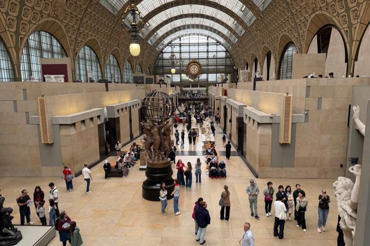 Interior of a grand museum hall with many visitors and sculptures.