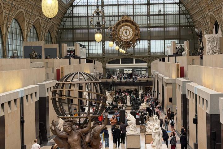 Crowded museum interior with sculptures and large clock in ornate hall.