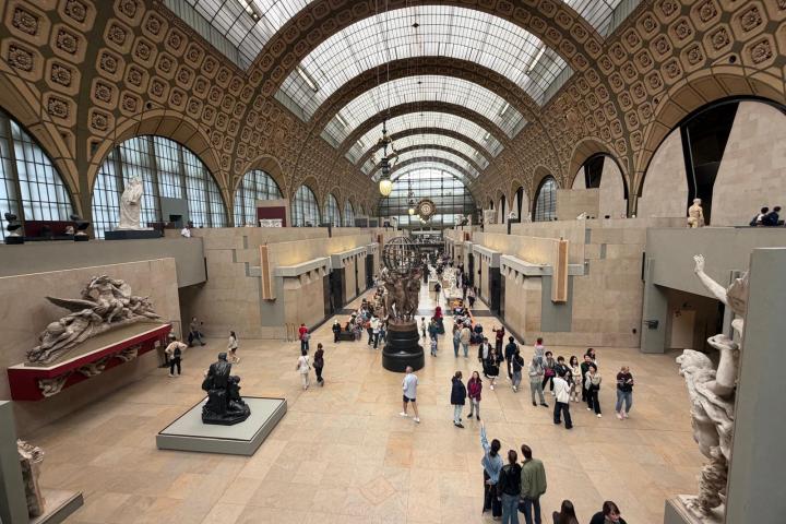People inside a large museum hall with arched glass ceiling and sculptures.